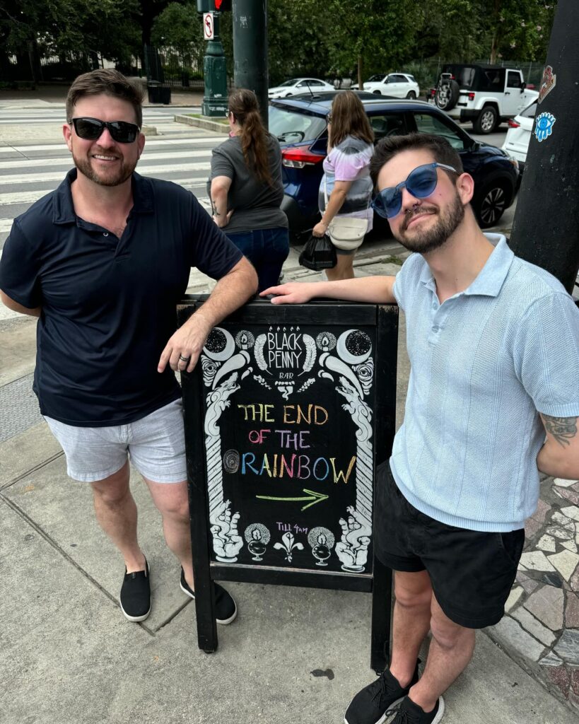 Chris and his husband beside a chalkboard sign in New Orleans